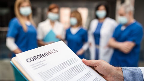 Corona-Impfung Blatt Papier mit der Aufschrift Coronavirus wird von einer Hand gehalten, im Hintergrund steht medizinisches Personal