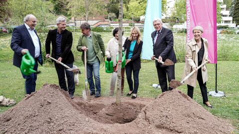 Ministerpräsident Bouffier mit Vertreterinnen und Vertretern des Landtages und der Stadt Wiesbaden, während er eine Schaufel in Händen hält und den Baum einpflanzt. 