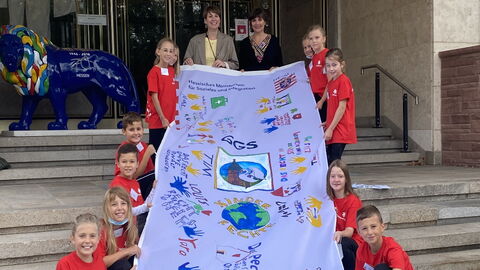 Schülerinnen und Schüler der Gönser Grundschule aus Butzbach übergeben die von ihnen gestaltete Fahne zum Thema Kinderrechte an die hessische Staatssekretärin für Soziales und Integration Anne Janz und die hessische Kinder- und Jugendrechtebeauftragte Miriam Zeleke
