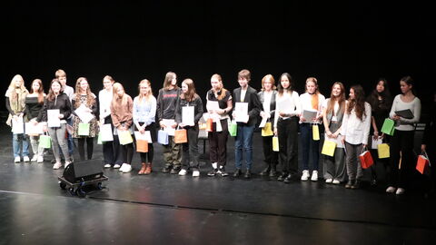 Mehrere Kinder und Jugenliche auf einer Bühne mit Urkunden und Papiertaschen in verschiedenen Farben