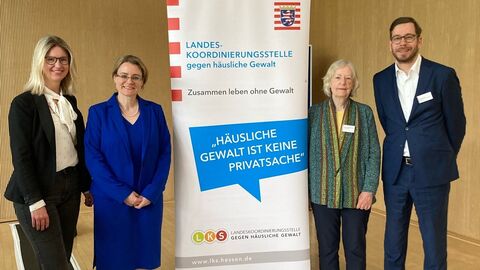 Julia Schäfer (HMdJ), Tanja Eichner (HMdJ), Prof. Dr. Margrit Brückner (Vorsitzende der AG „Gewalt im häuslichen Bereich“) und Michael Achtert (HMdJ) stehen zusammen neben einem Aufsteller mit der Aufschrift "Häusliche Gewalt ist keine Privatsache".  