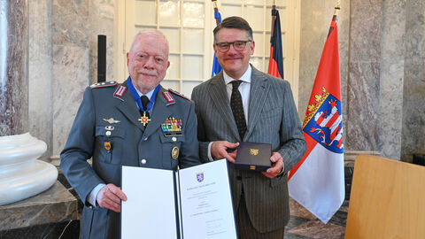 Zwei Männer stehen nebeneinander und halten eine Urkunde hoch.