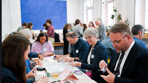 Kulturminister Gremmels sitzt mit anderen Personen an einem Tisch und hält Papier in der Hand.
