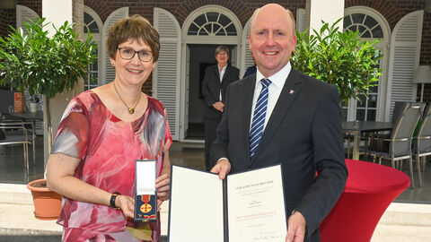 Marion Beier und Europastaatssekretär Uwe Becker halten Verdienstmedaille und Urkunde in die Kamera
