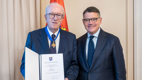 Zwei Männer stehen nebeneinander. Der linke hält eine Urkunde hoch.