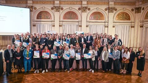 Über 30 Menschen stehen nebeneinander in einer Halle und halten ihre Urkunden in der Hand.
