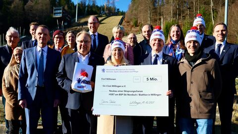 Eine Gruppe von knapp 20 Personen steht am Fuße einer Skisprungschanze - die forderen halten einen Förderbescheid in den Händen.