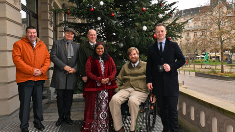 Sechs Personen nebeneinander vor einem dezent geschmückten Weihnachtsbaum